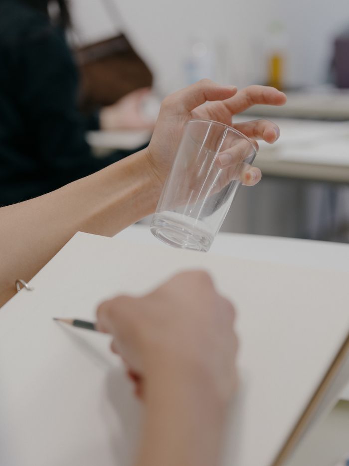 A close-up view of a person holding a glass while sketching, captured during an art class session.